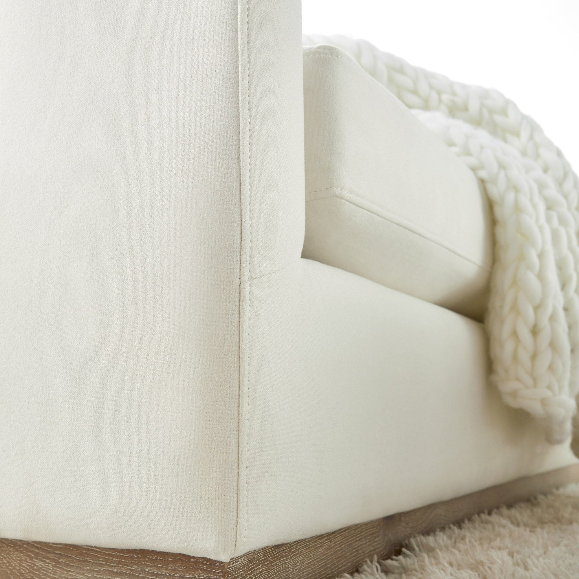 Close-up of ivory sofa corner upholstered in soft LiveSmart fabric with a chunky knit throw on wood plinth base by Essentials for Living