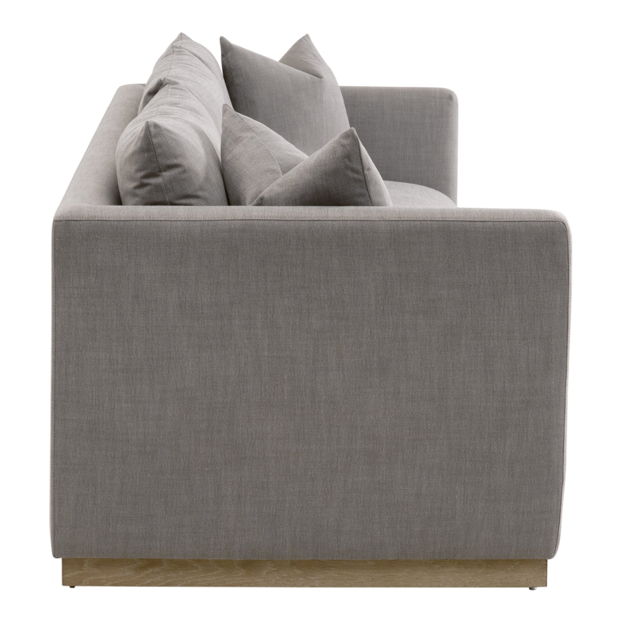 Side view of a gray upholstered sofa with plush cushions and exposed wood plinth base in a modern style