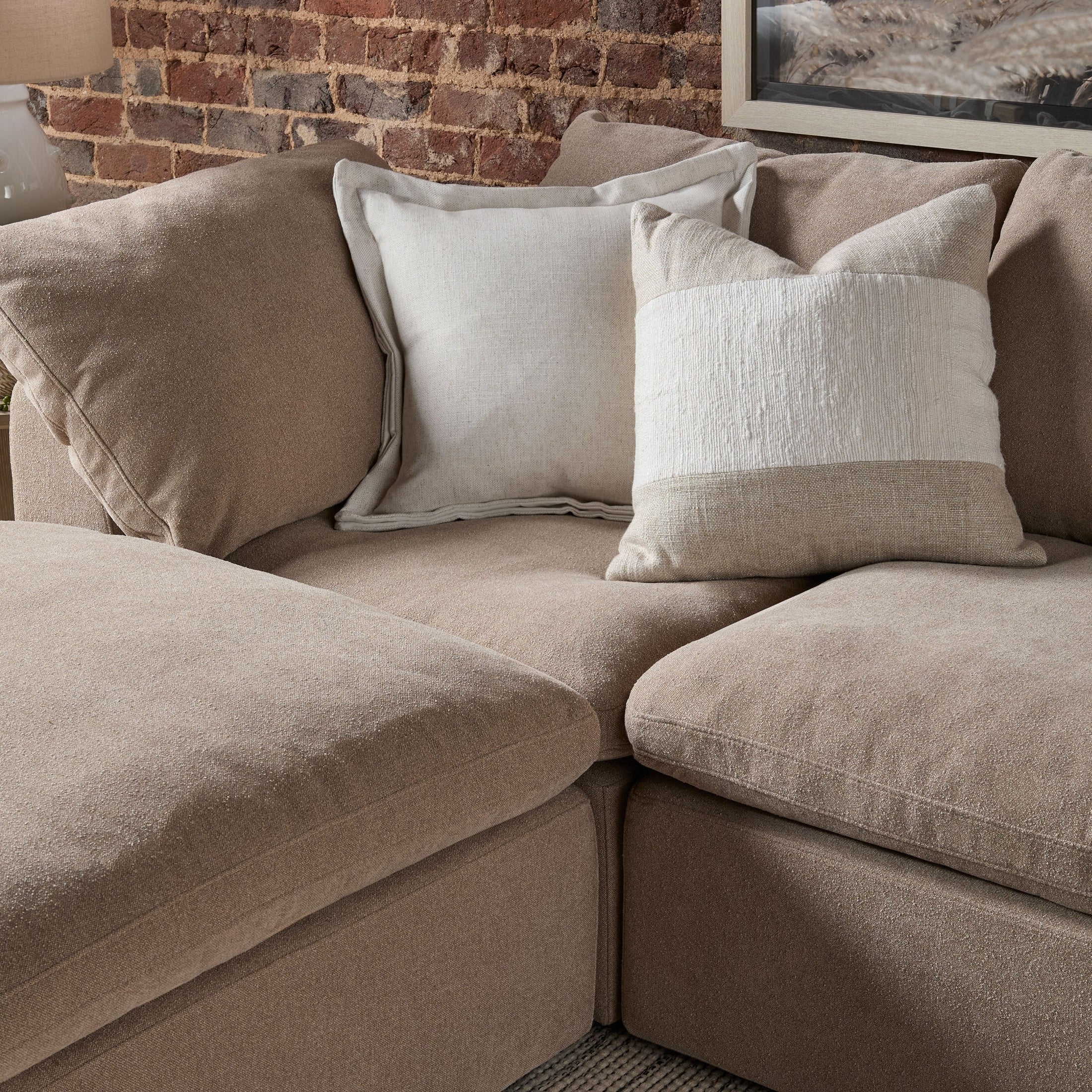 Close-up of beige modular armless chair corner with textured pillows against exposed brick wall background