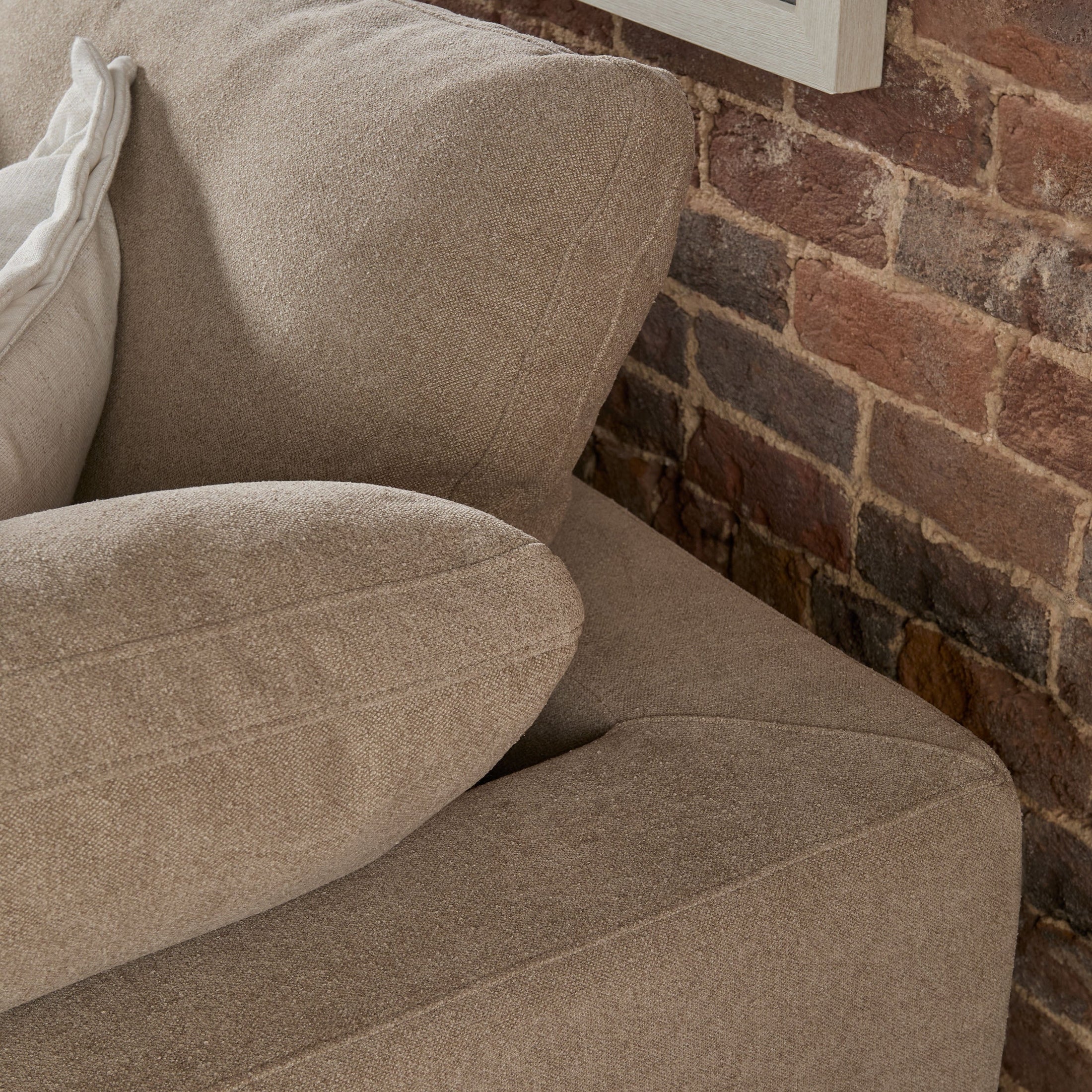 Close-up of a beige modular corner chair with plush cushions against an exposed brick wall background