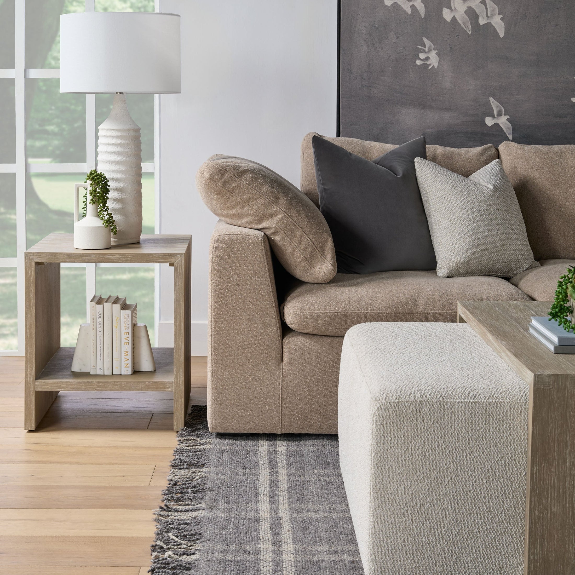 Essentials for Living beige sectional sofa with plush pillows next to a wooden side table with lamp and books