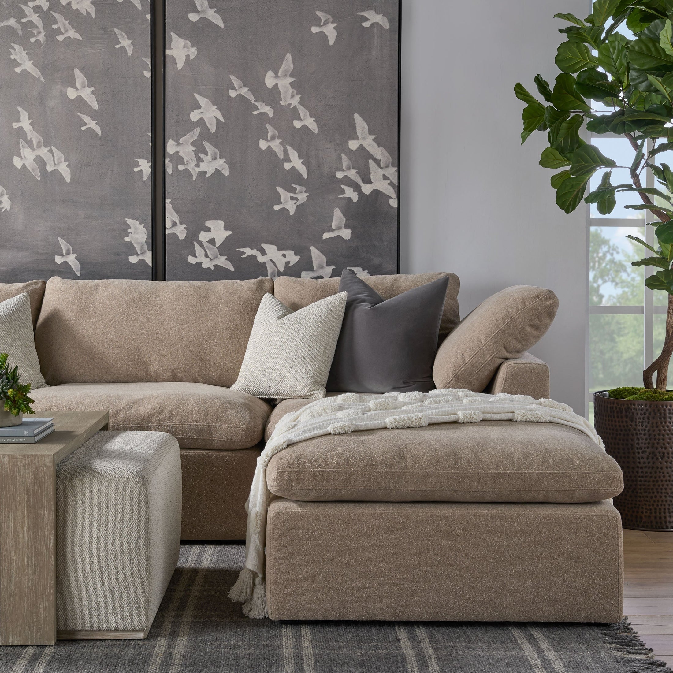 Beige modular ottoman with plush cushion and throw, styled in modern living room with sectional sofa and wall art