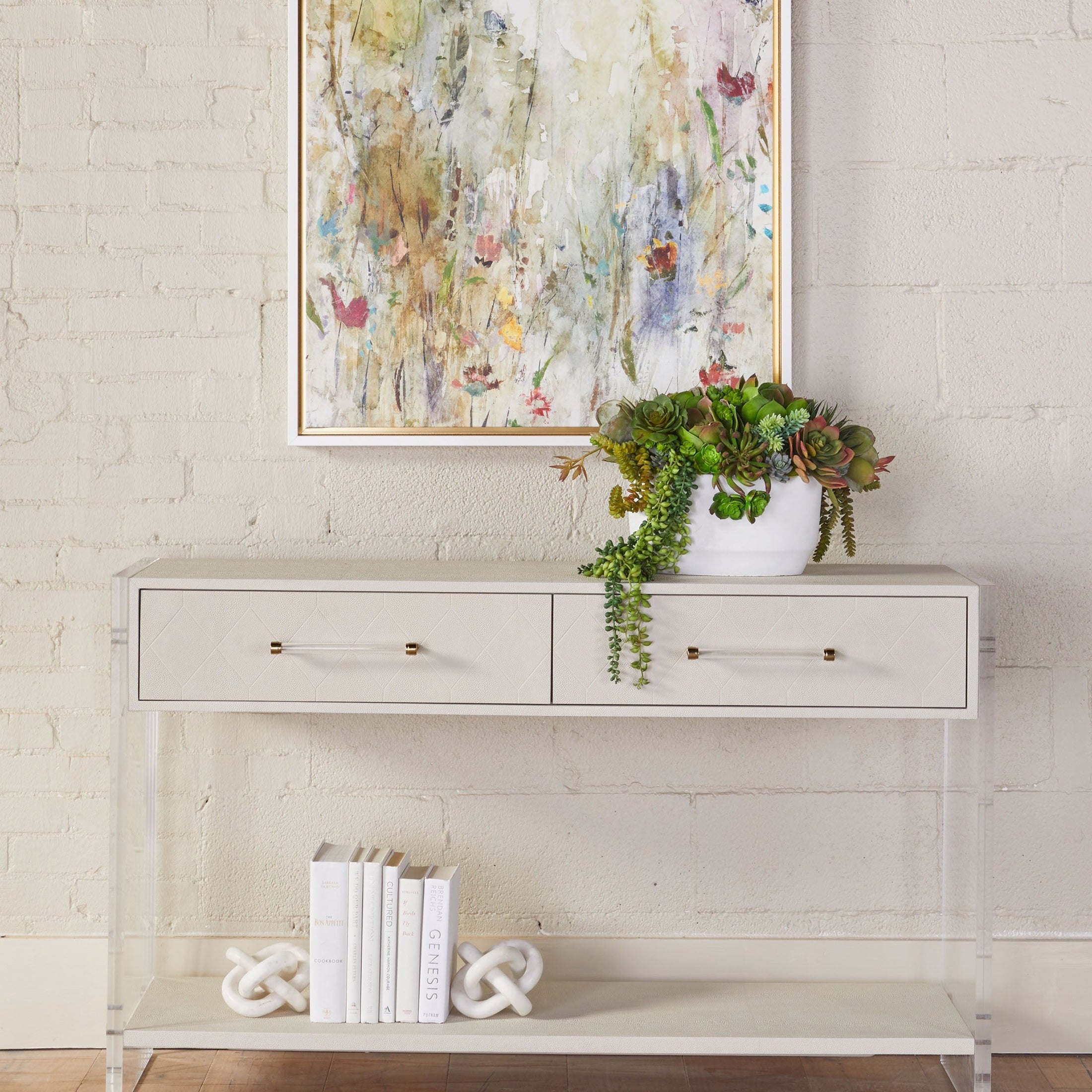 Pearl white Sonia Shagreen Console Table with acrylic legs, brass accents, two drawers, and open lower shelf styled with plants and books