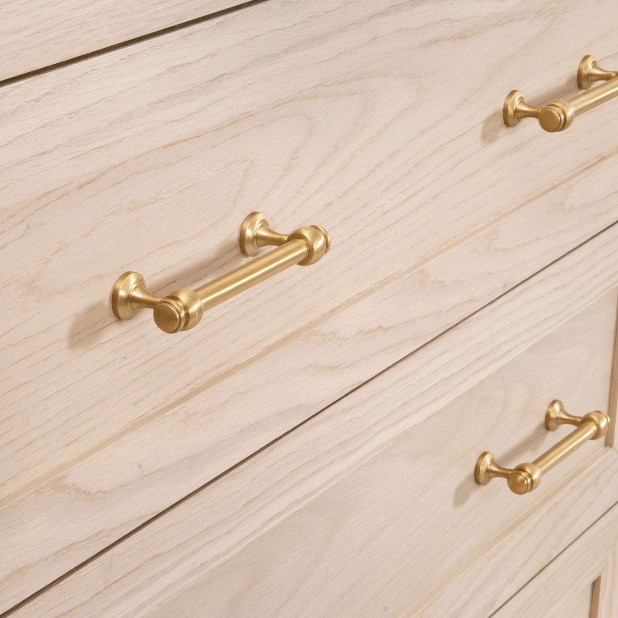 Close-up of brushed brass handles on light wood dresser drawers by Essentials for Living in transitional style