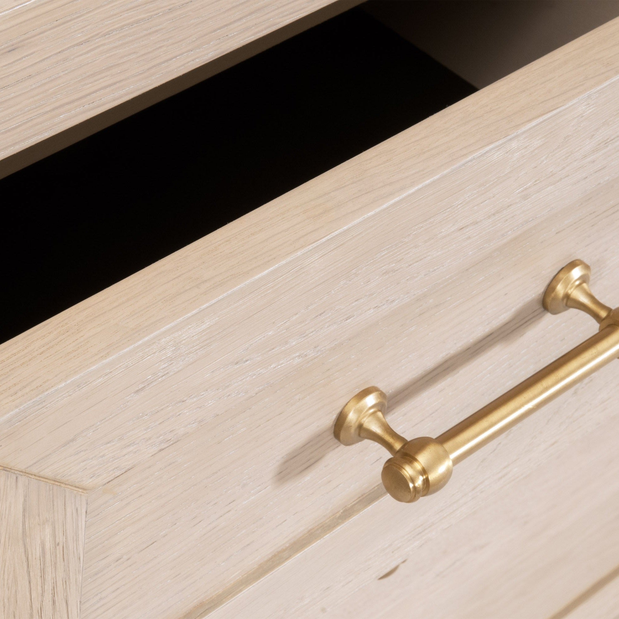 Close-up of open drawer on a light wood high chest featuring brushed brass handle and smooth edge detailing