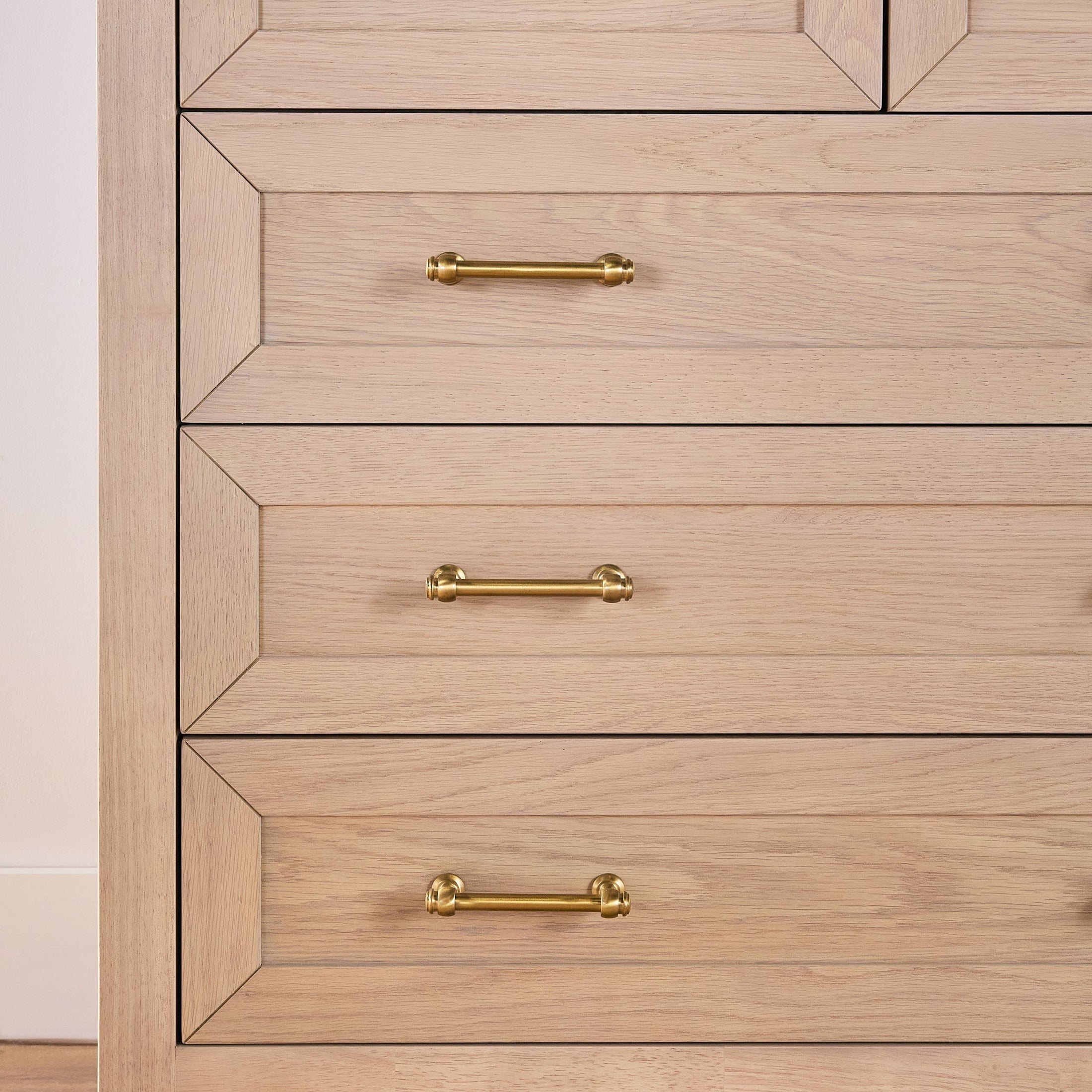 Close-up of natural wood dresser drawers with elegant brushed brass handles in a modern transitional design