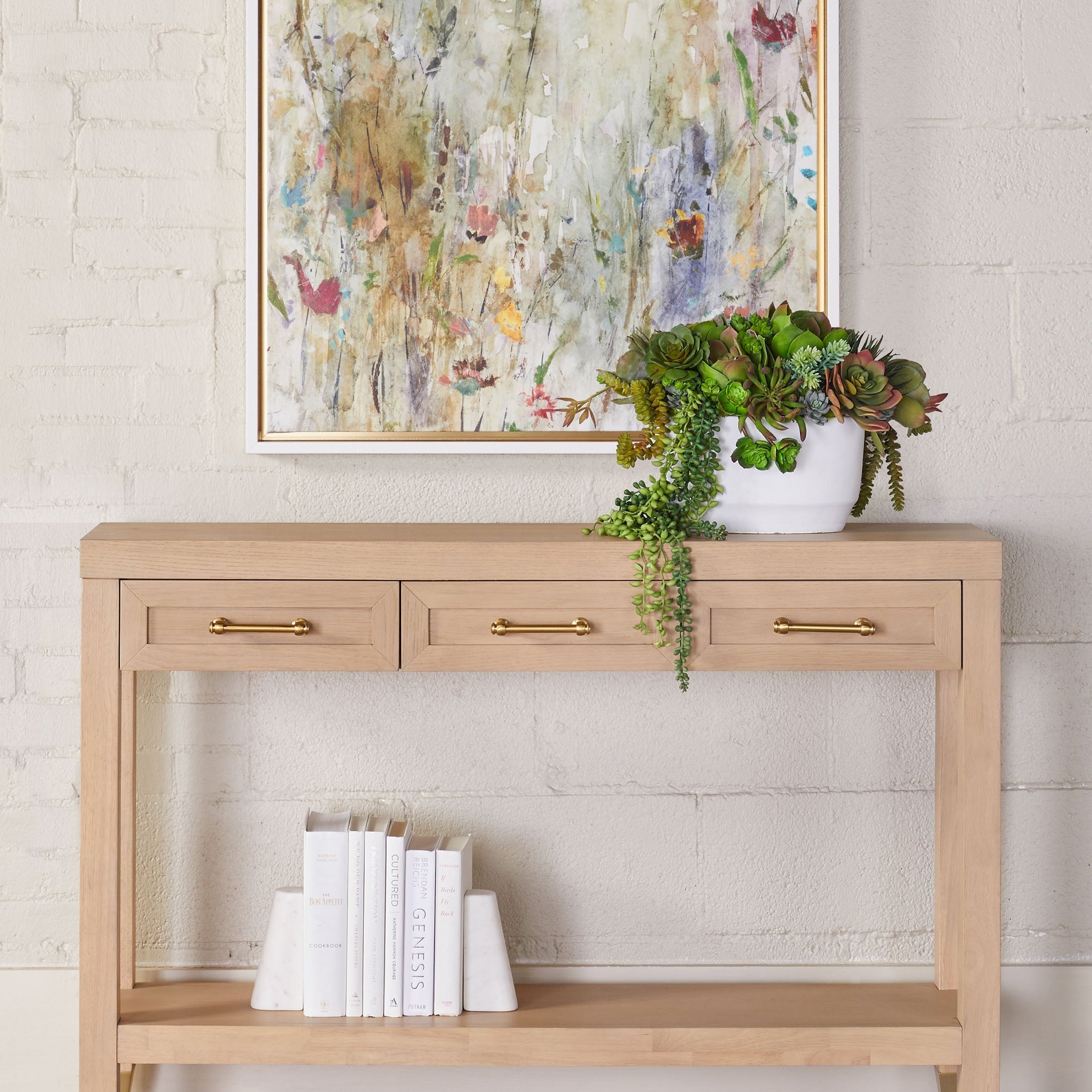 Essentials for Living Stella Narrow Console Table in light honey oak with brass hardware, three drawers, and a lower shelf with décor