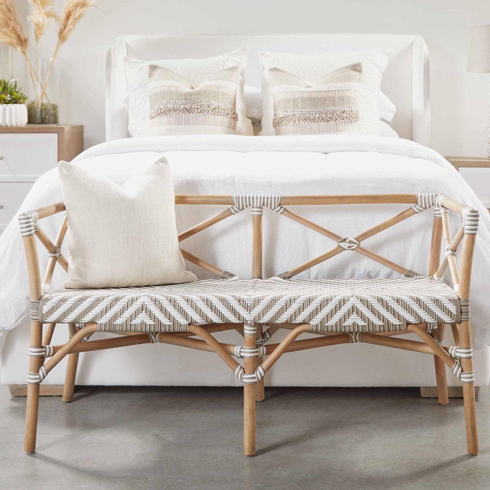 Natural gray oak bench with woven seat and decorative pillow placed in front of a white upholstered king bed