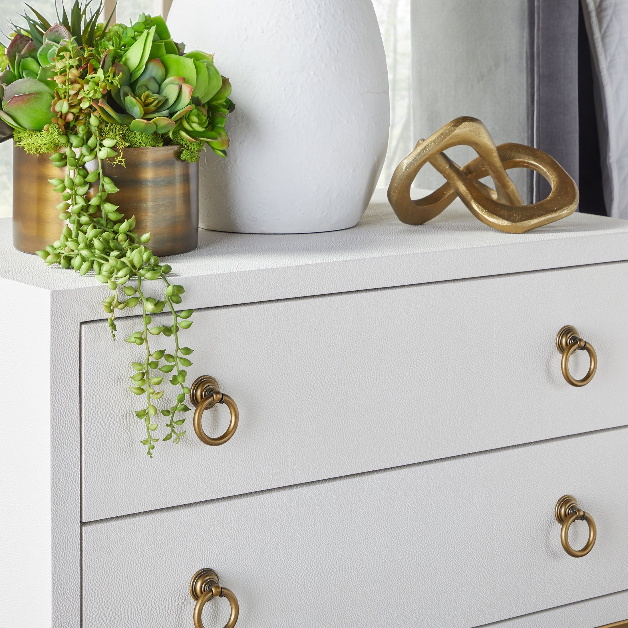 Close-up of gray Strand Shagreen 2-drawer nightstand with brass ring pulls and decorative items on top