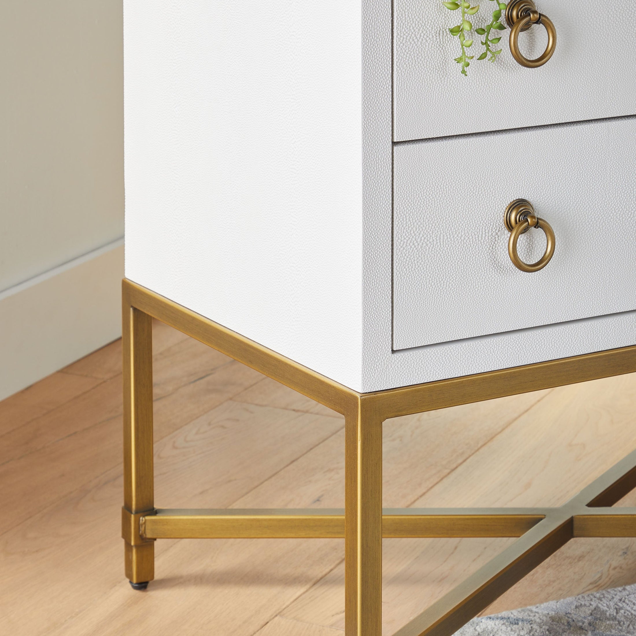 Close-up of a gray faux shagreen nightstand with brass ring pulls and a brushed gold metal base on wood floor