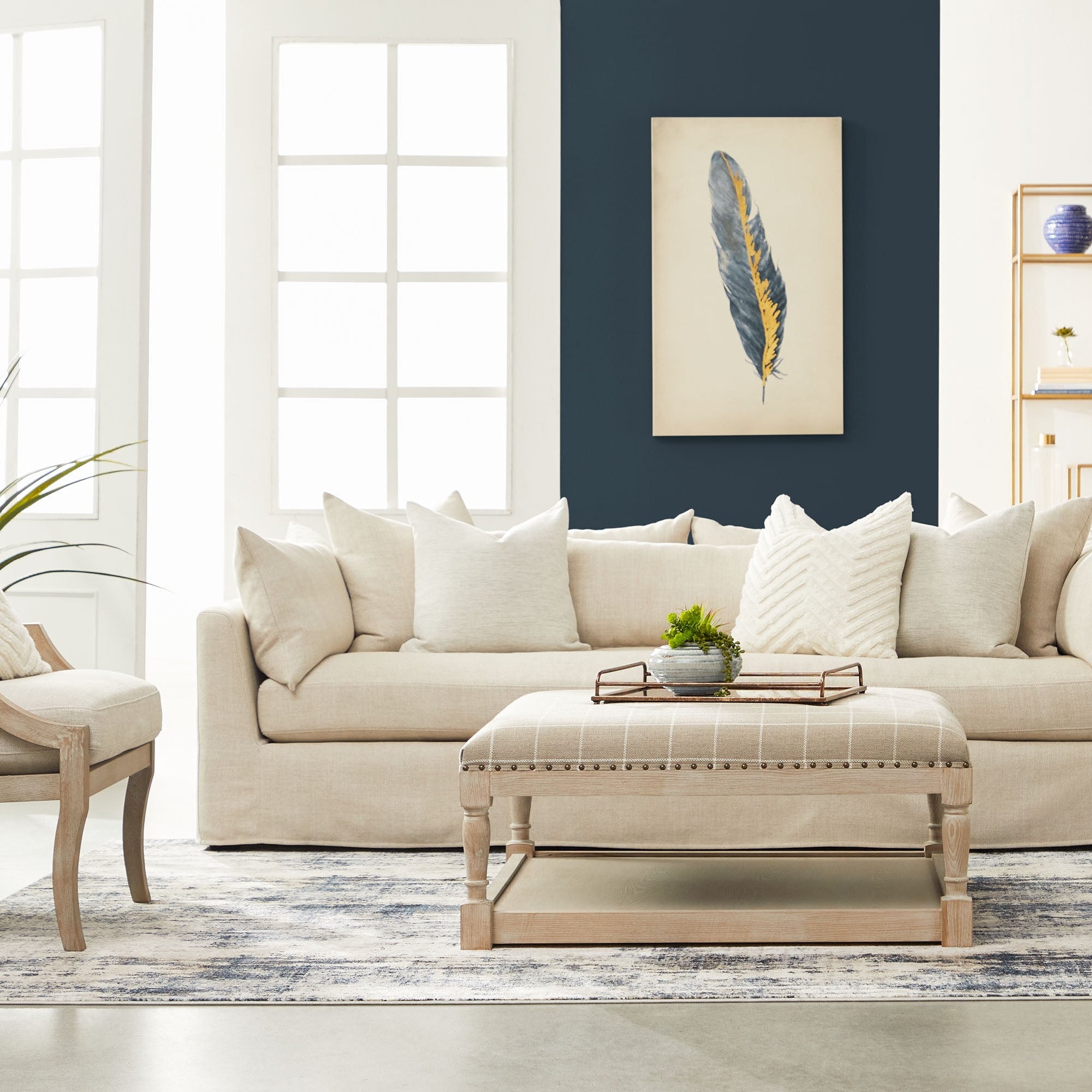 Neutral-toned living room with a beige sofa, matching ottoman, and an armchair featuring natural wood frames.