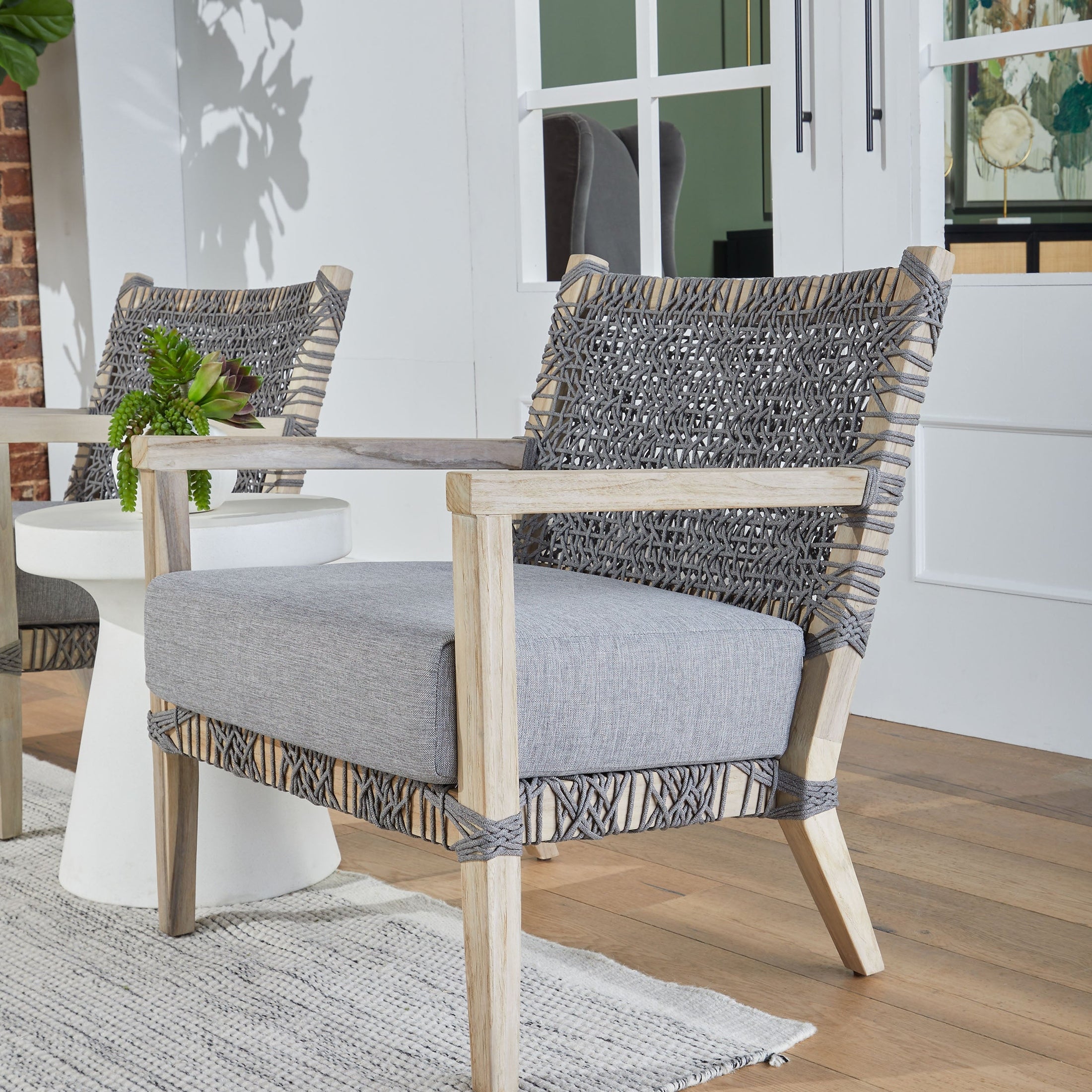 Modern woven accent chair with wooden frame and gray cushion on hardwood floor near white table