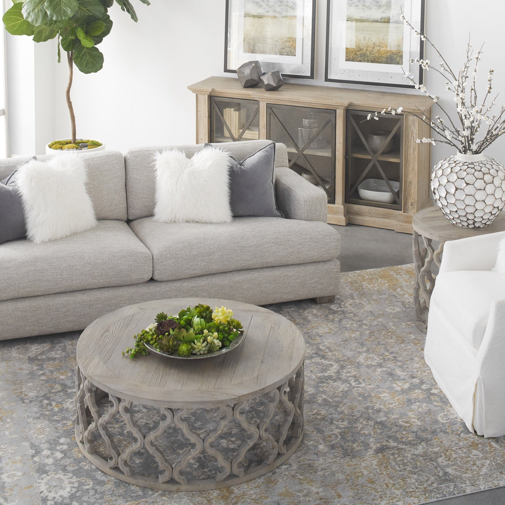 Living room with neutral sofa, textured round coffee table, and decorative cabinet under framed artwork