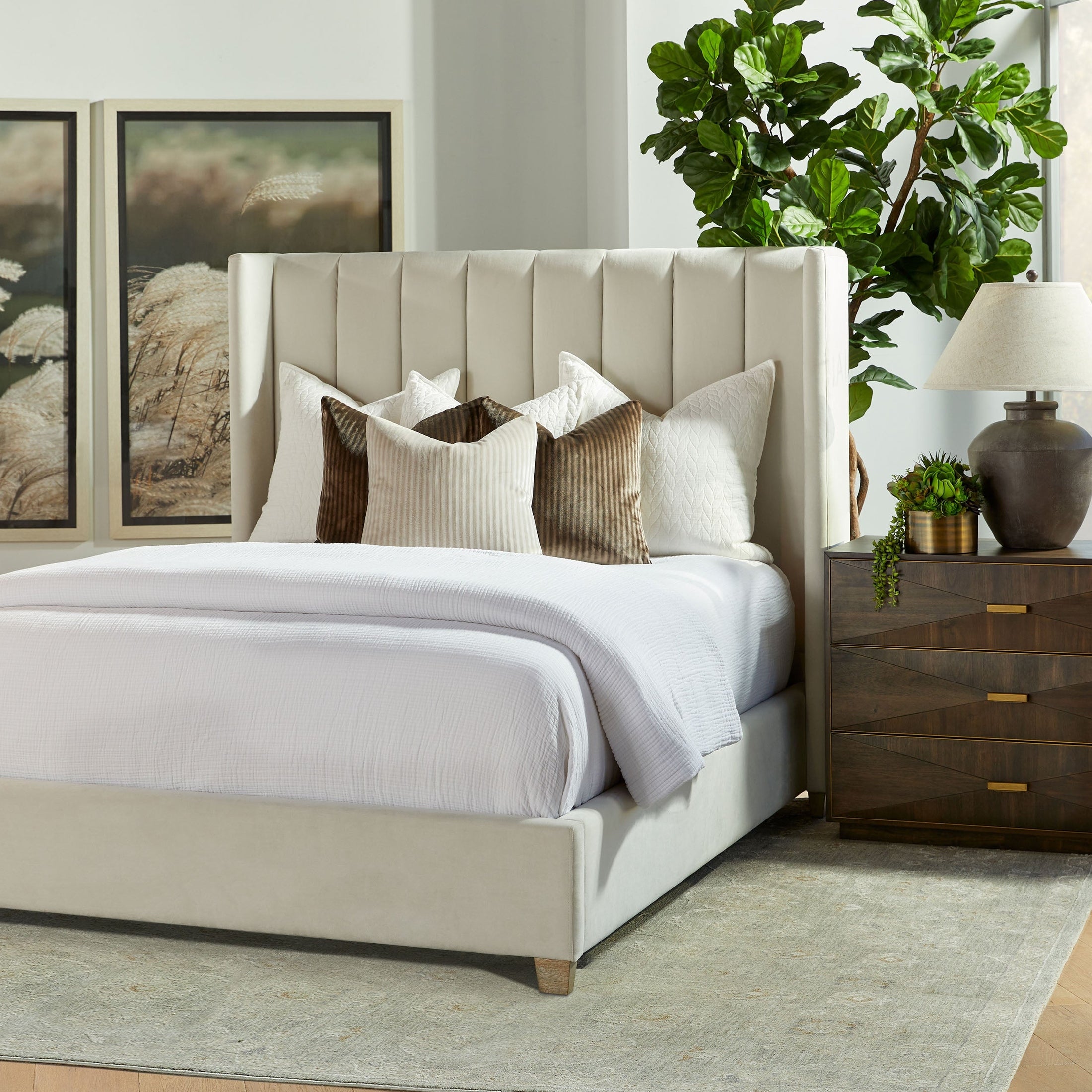 Wynn nightstand by Essentials for Living with burnished brown acacia veneer, 3 drawers, and brushed gold handles beside a bed.
